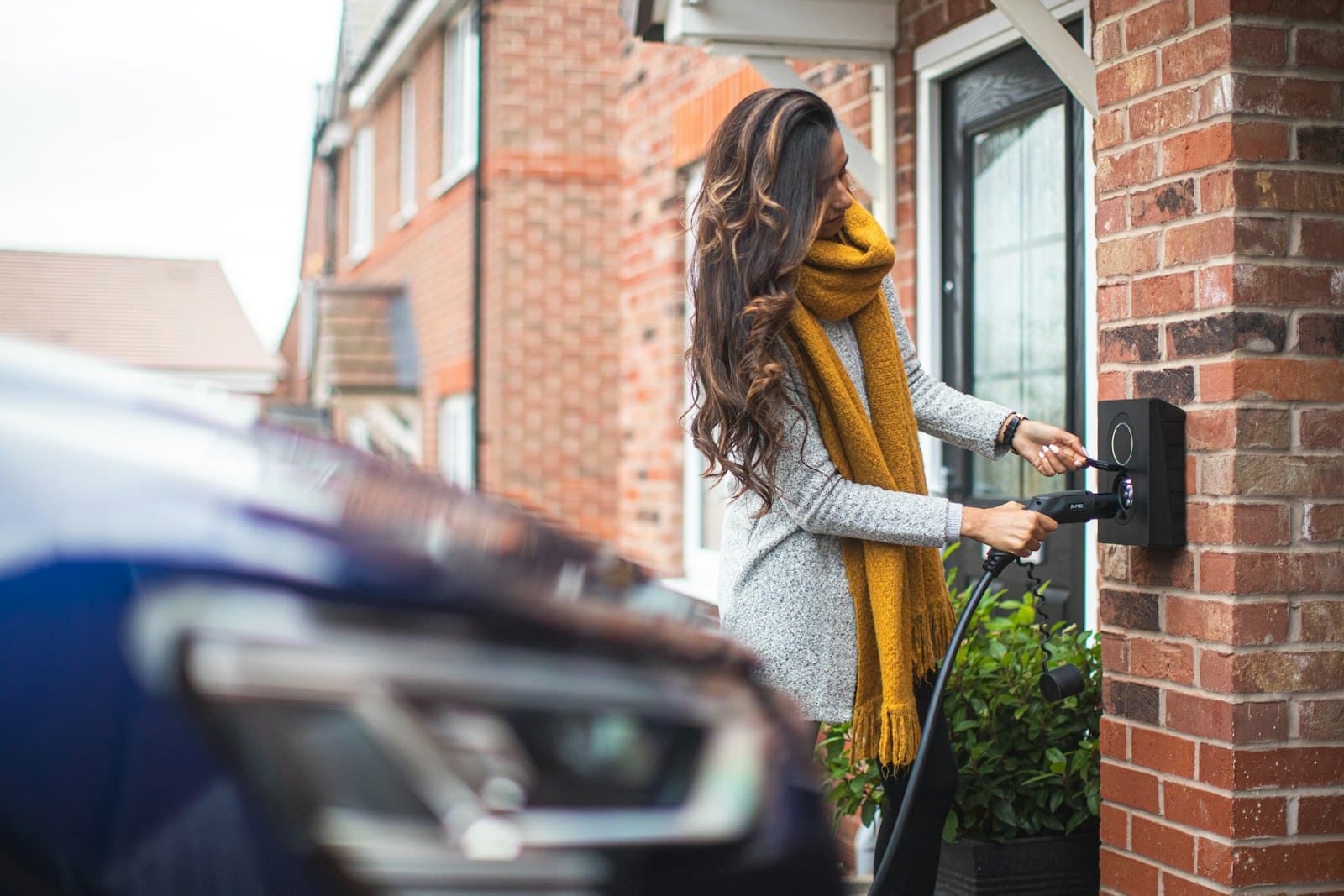 Vrouw start een laadsessie bij de laadpaal aan de gevel